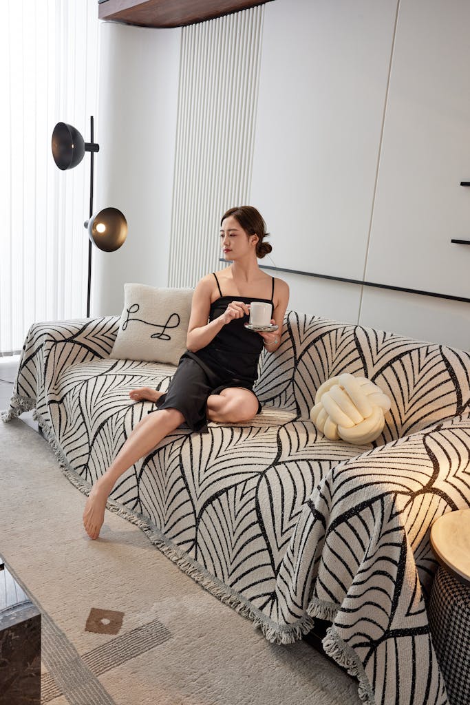 Woman in chic home interior enjoying coffee on a patterned couch.
